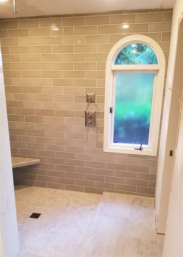 Glass-enclosed tile shower with teak bench and matte black fixtures